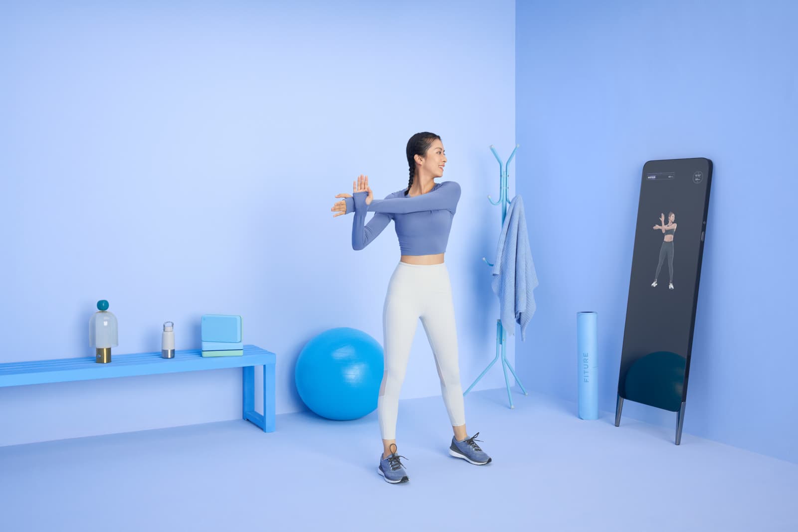 Fitness tech advertising with woman stretching in styled blue studio with smart workout mirror by Una Zhu