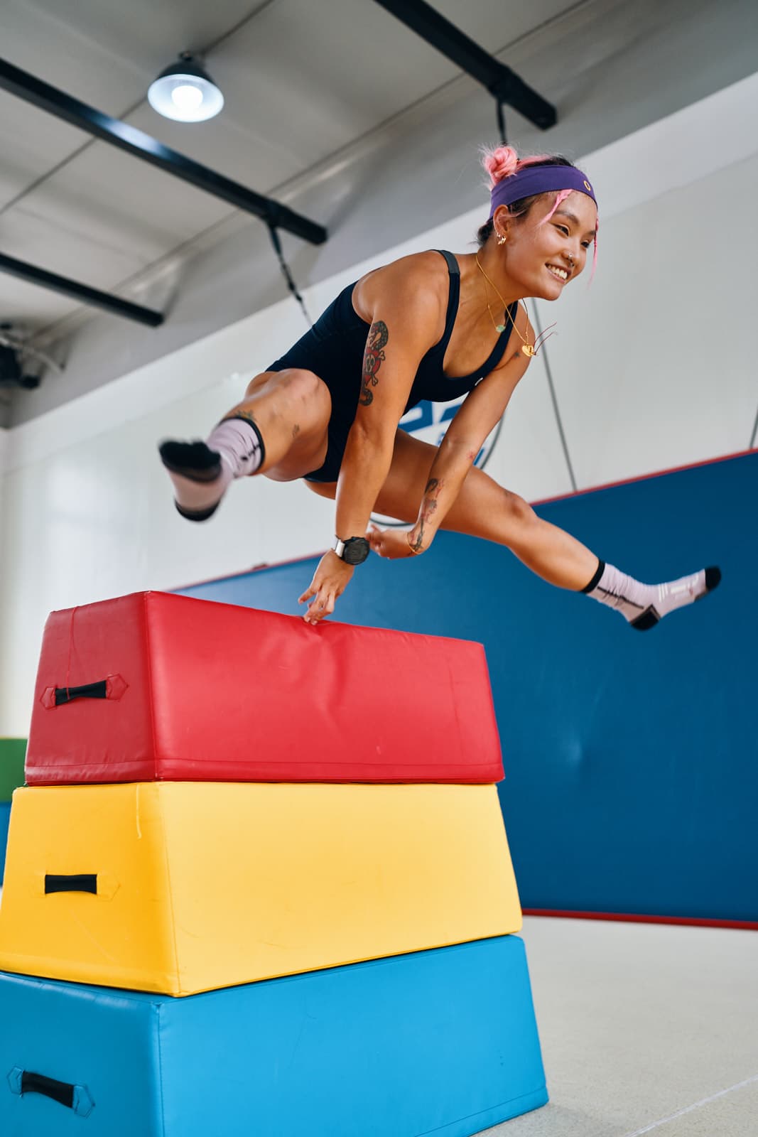 Lifestyle fitness editorial with athlete vaulting over colorful gym boxes in dynamic action shot by Una Zhu