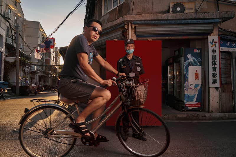 Street documentary portrait of cyclist and security guard with red backdrop in Shanghai alley at golden hour by Una Zhu