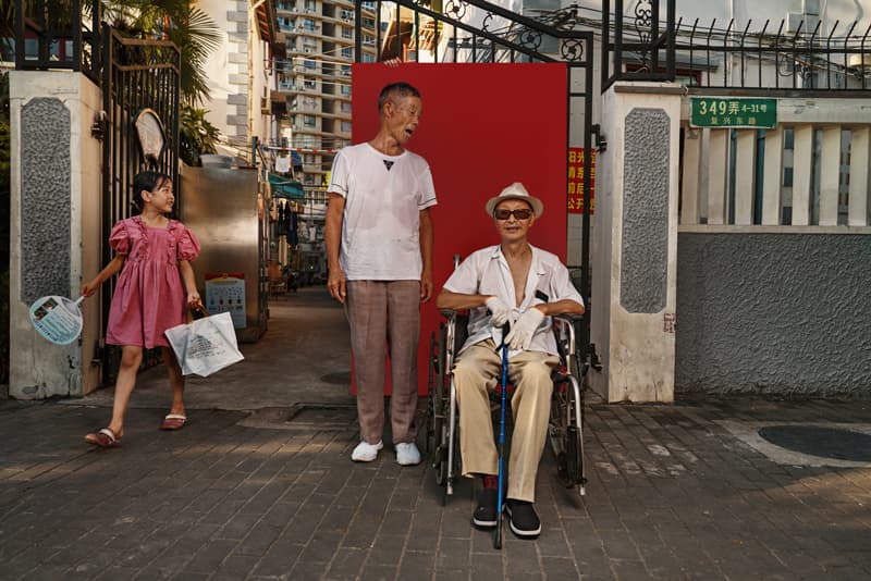 Documentary portrait of elderly neighbours laughing together against red backdrop in Shanghai lane by Una Zhu