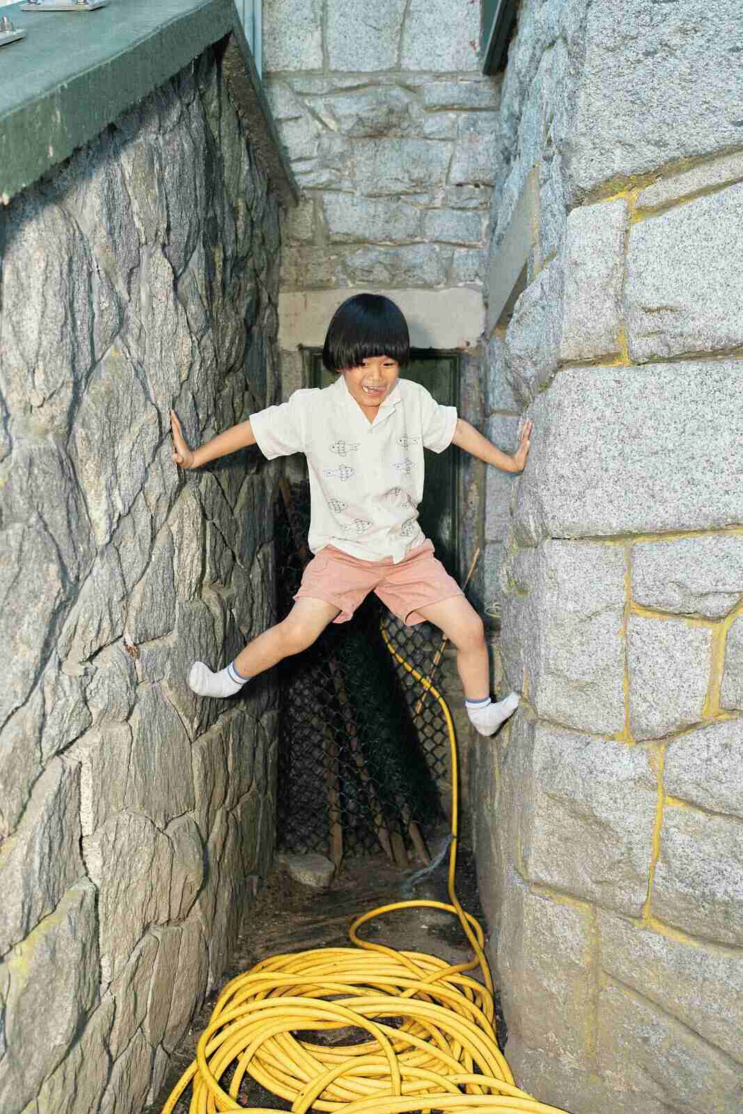 Candid photo of a boy jumping between stone walls during a play session in Vancouver by Una Zhu