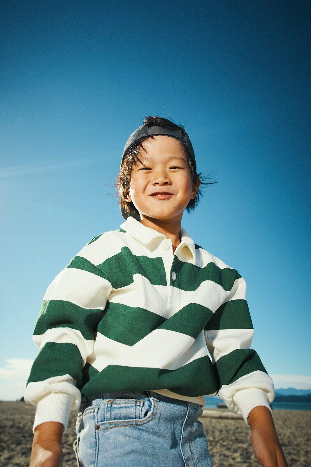 Candid beach photo of a child squinting into the sun against a clear blue sky in Vancouver by Una Zhu
