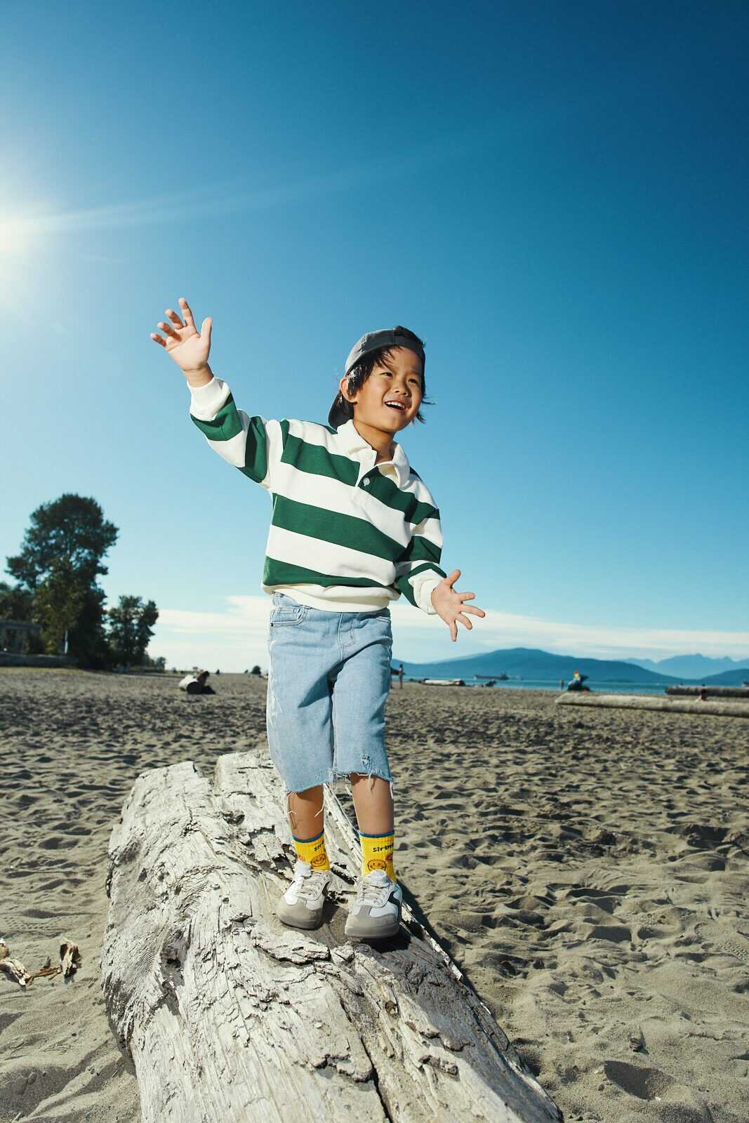 Candid photo of a child balancing on beach driftwood with arms out in Vancouver by Una Zhu