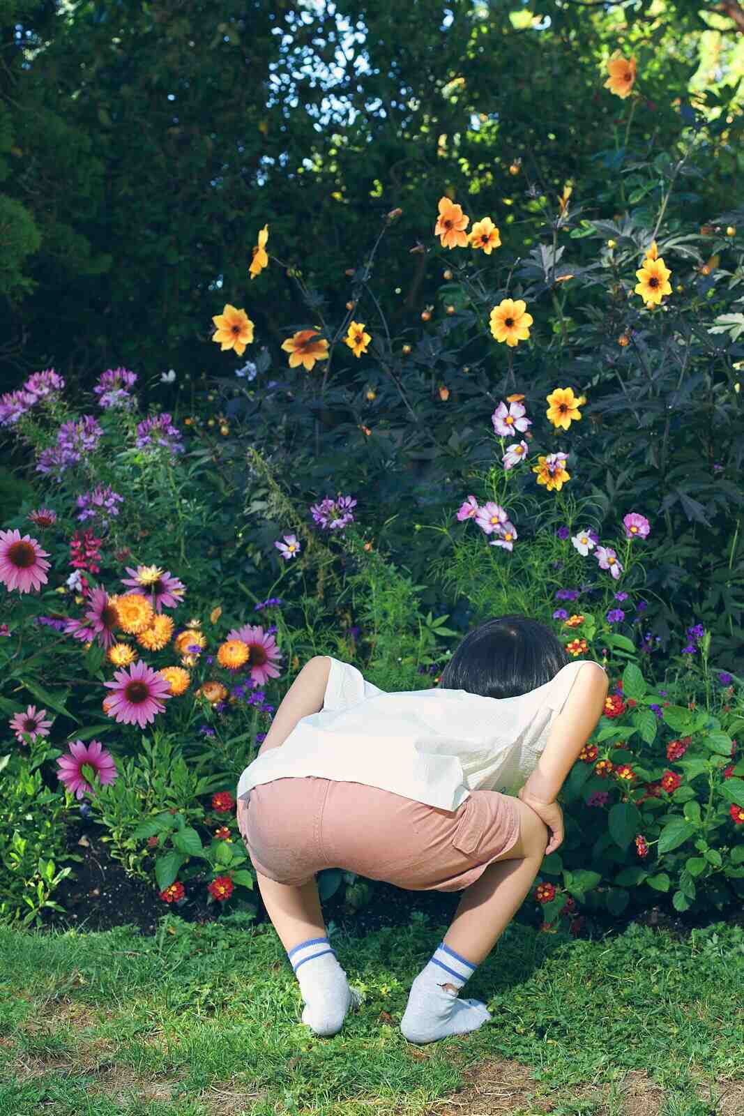 Candid kids photography of a child bent over exploring a flower bed in Vancouver, not looking at the camera, by Una Zhu