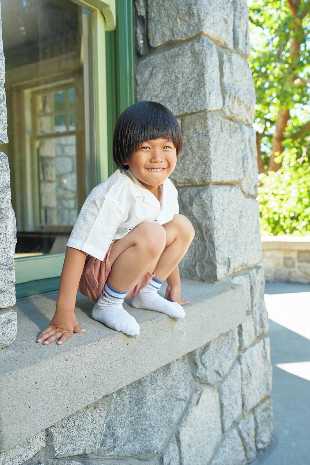 Candid photo of a boy crouching on a stone window ledge mid play during a Vancouver play session by Una Zhu