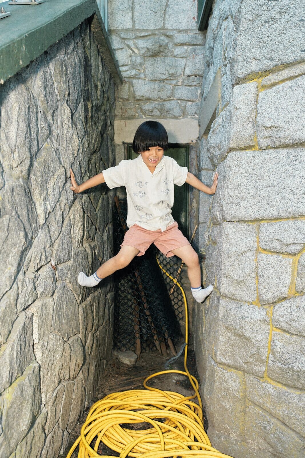 Candid photo of a child braced between two stone walls mid climb during a Vancouver play session by Una Zhu