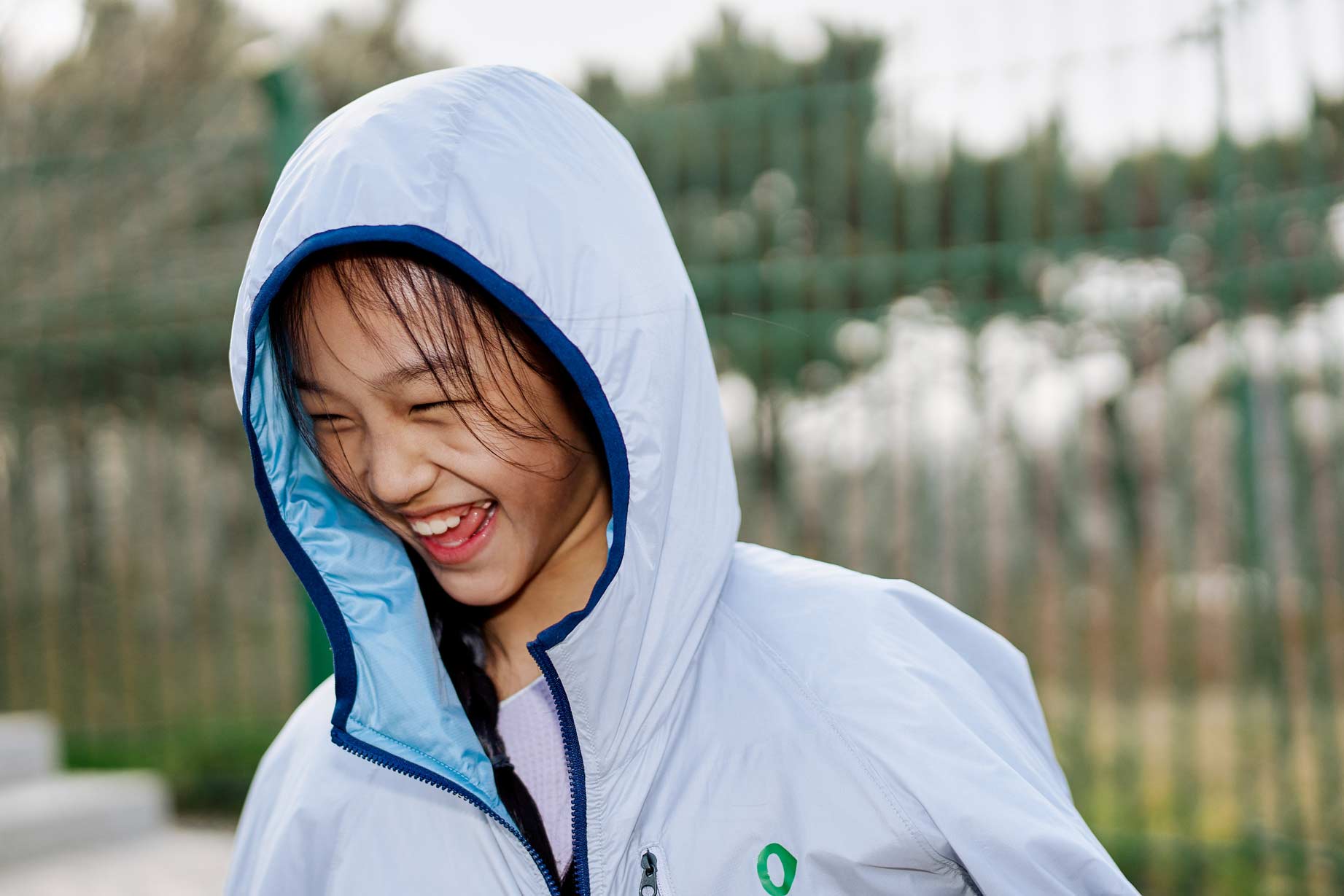 Lifestyle kids apparel advertising with child laughing in hooded jacket outdoors by Una Zhu