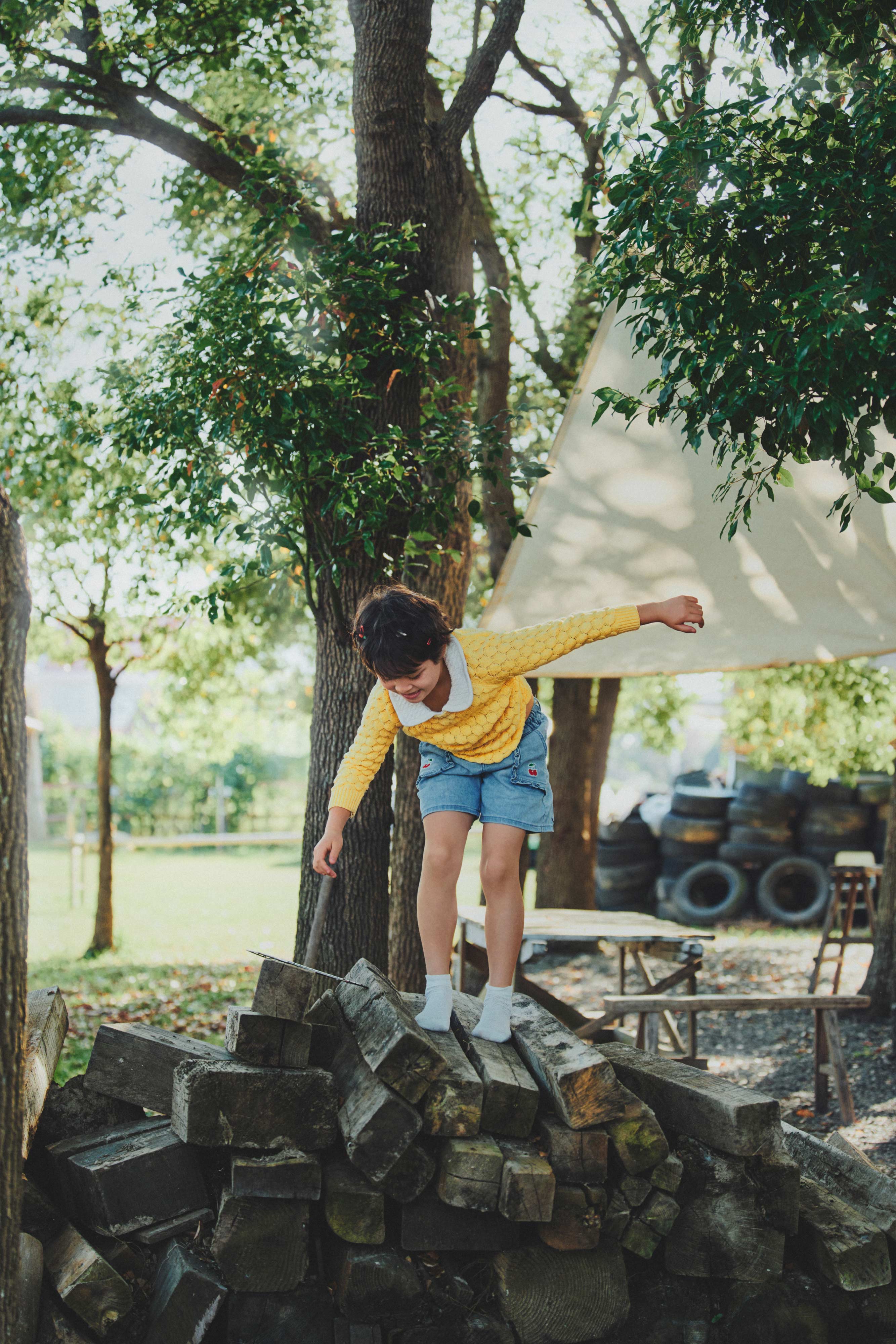 Natural light kids editorial photography with child balancing on woodpile outdoors by Una Zhu